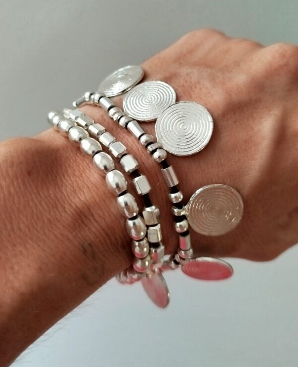 Bracciale a tre fili con perle color argento, perle placcate argento e piccoli medaglioni rotondi per un look bohémien. Ideale per chi ama lo stile etnico e desidera un accessorio unico e versatile.