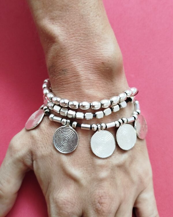 Bracciale a tre fili con perle color argento, perle placcate argento e piccoli medaglioni rotondi per un look bohémien. Ideale per chi ama lo stile etnico e desidera un accessorio unico e versatile.
