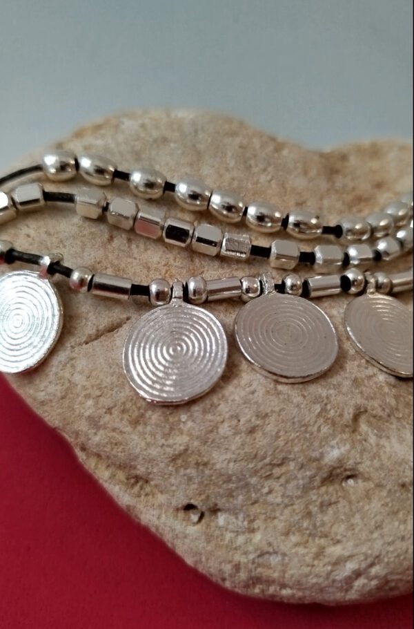 Bracciale a tre fili con perle color argento, perle placcate argento e piccoli medaglioni rotondi per un look bohémien. Ideale per chi ama lo stile etnico e desidera un accessorio unico e versatile.
